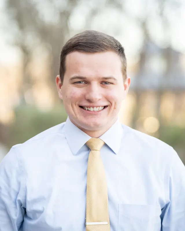 Michael Pitts smiling, wearing a light blue shirt and gold tie